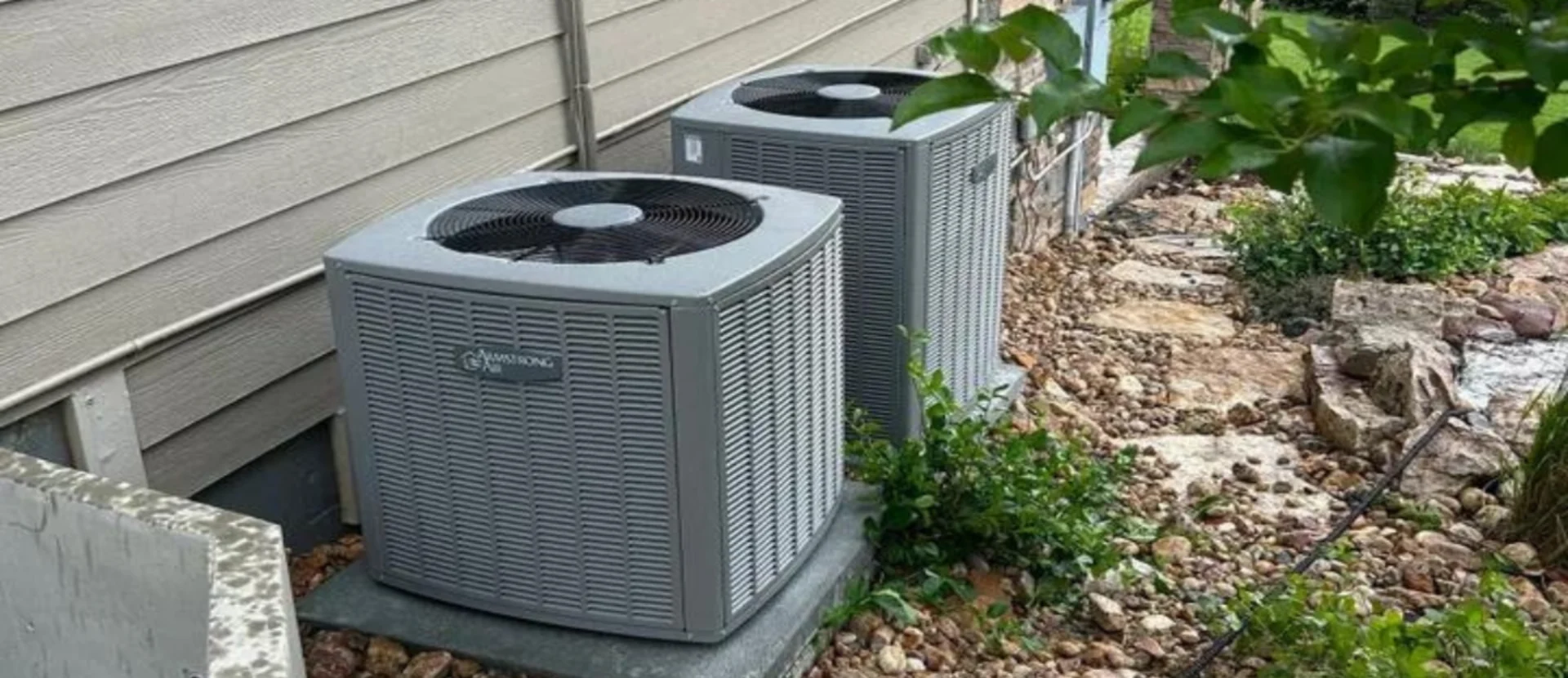 Two air conditioners are sitting outside on the ground.